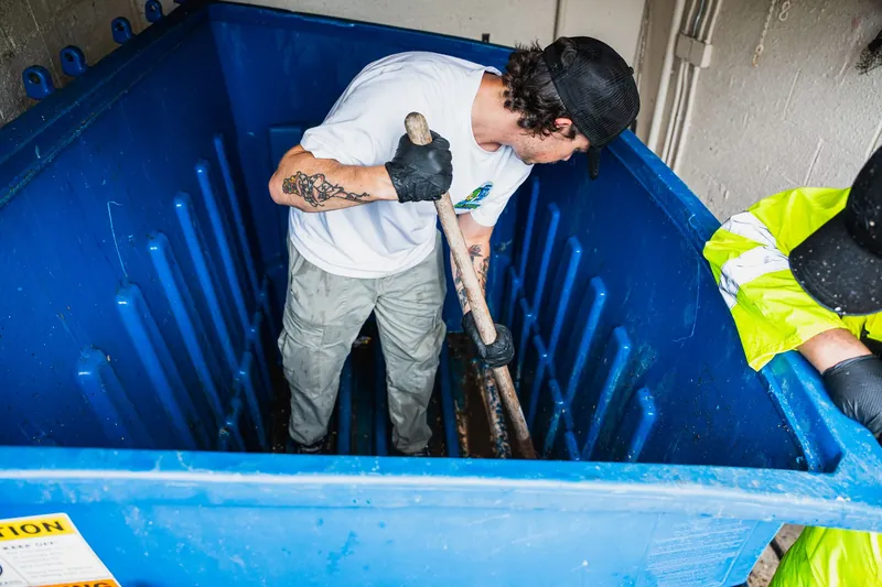 Crew member standing inside a dumpster scrubbing the walls