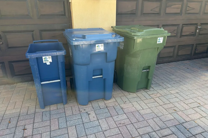 Three clean bins lined up at the garage on a paver driveway