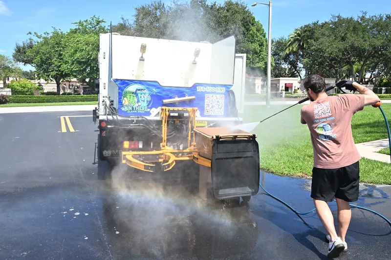 Bin There Clean That crew pressure washing a trash can on the truck lift